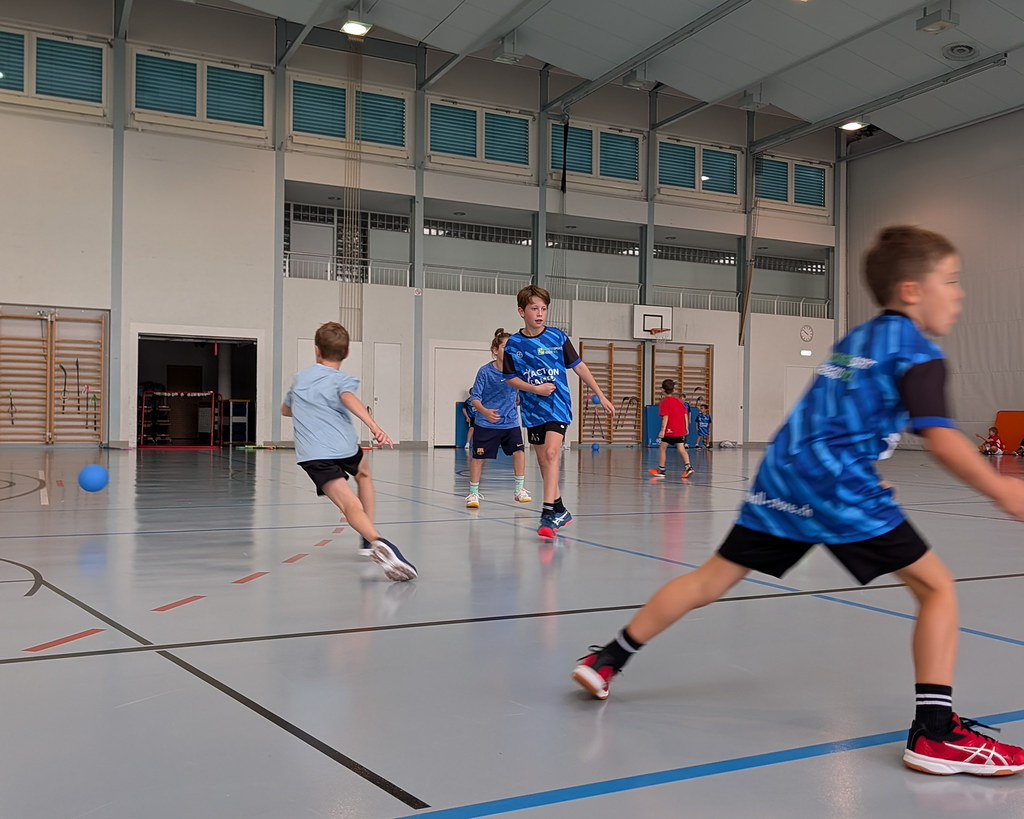 Kinder spielen gemeinsam Unihockey in der Sporthalle.