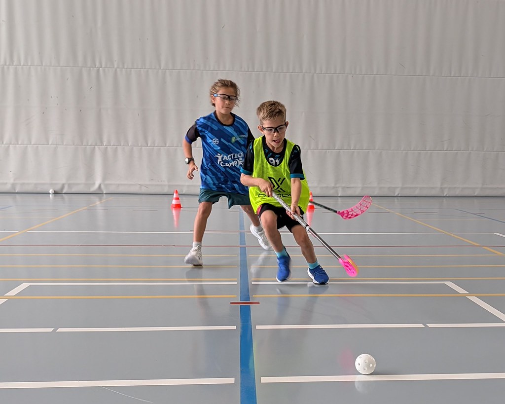 Zwei Kinder spielen mit Unihockeystöcken um den Ball.